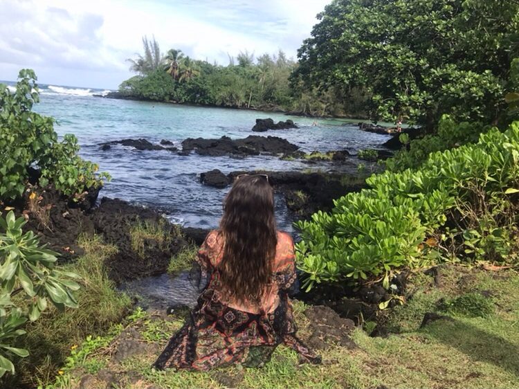 Emily sitting on the shoreline overlooking a lush Hawaiian cove
