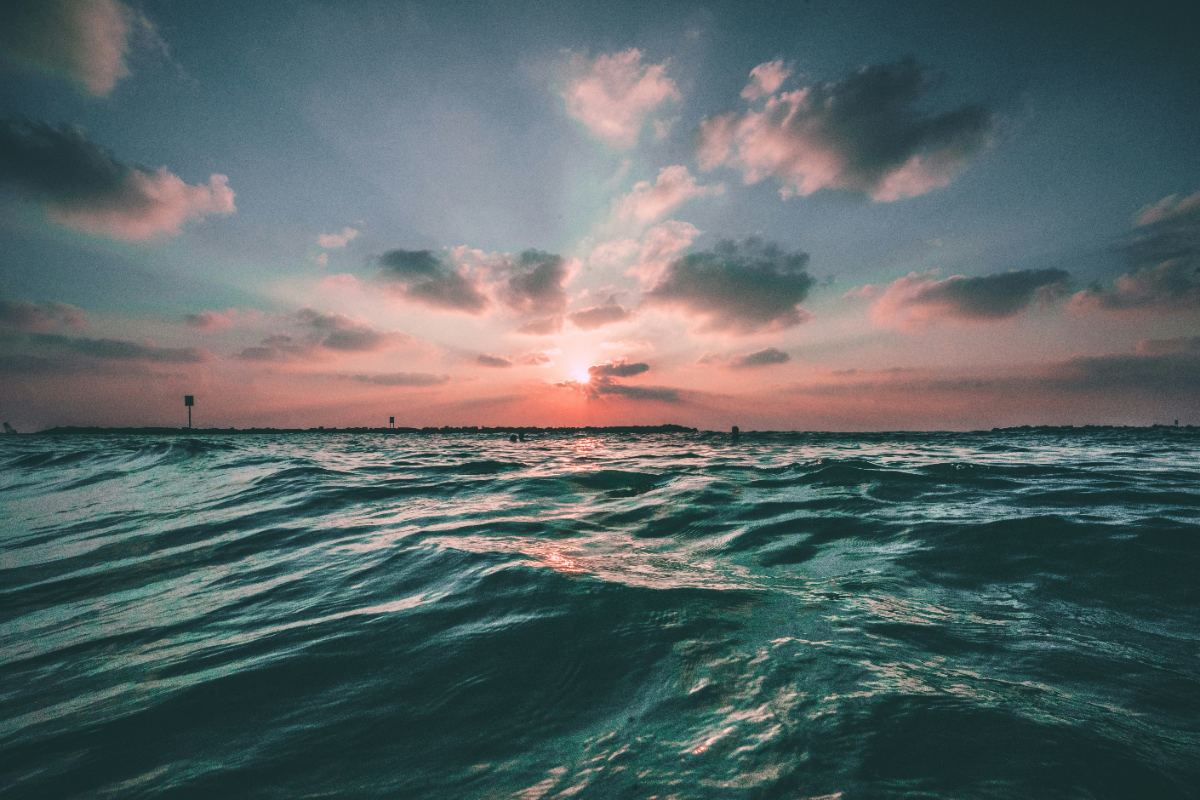 Waves at sunset with swimmers silhouetted against the horizon