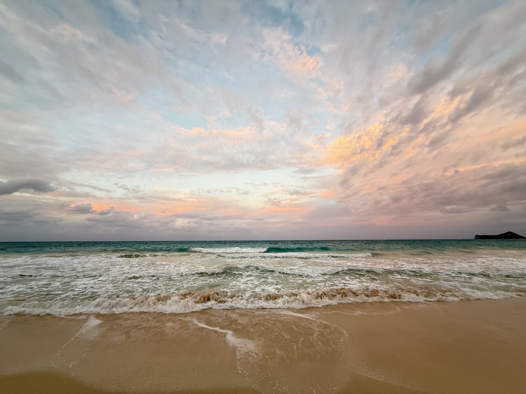 Soft pink clouds over a quiet shoreline at dusk