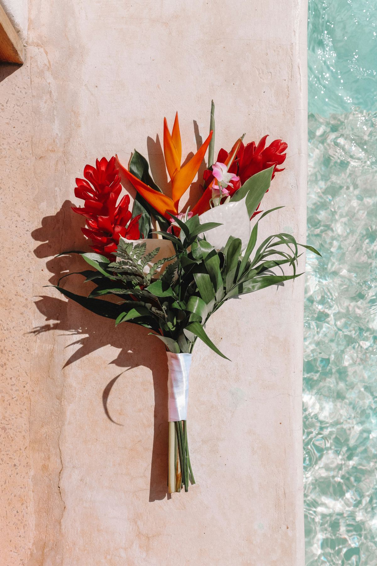 A tropical bouquet of ginger, heliconia and orchids beside a turquoise pool